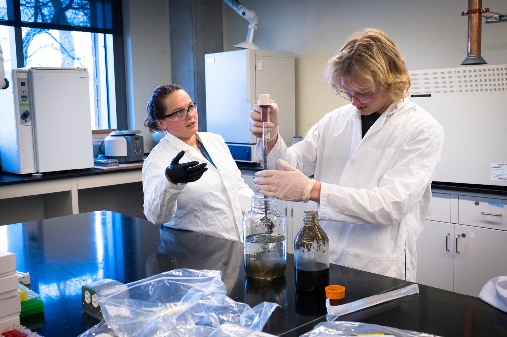 Two students work in a lab as one uses a pipette in a project.