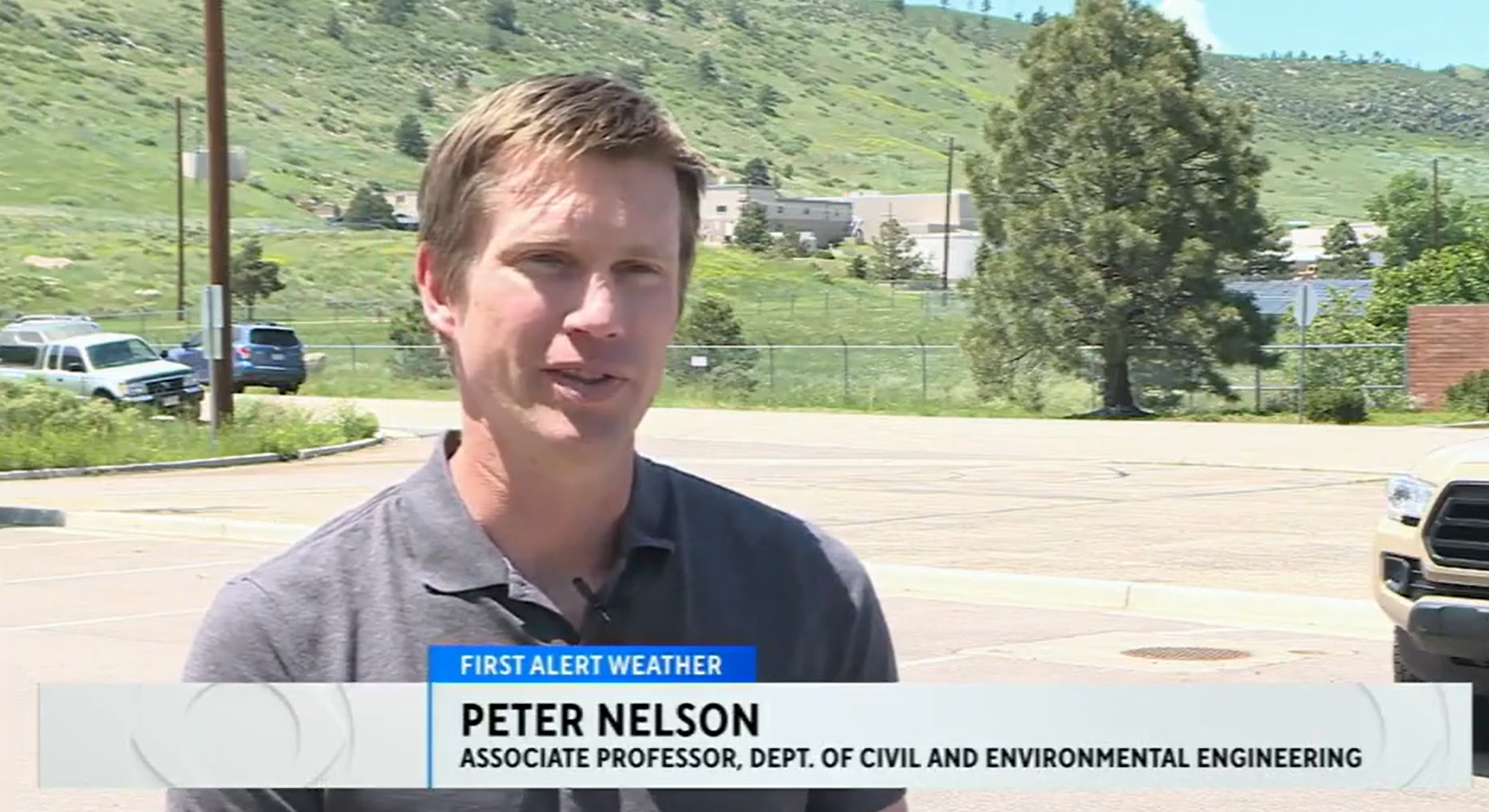 Man giving TV interview in front of grassy hill
