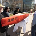 Students holding an orange concrete canoe with "Colorado State" painted on the side.