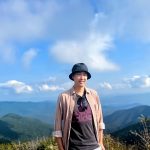 Man wearing a hat poses in front of mountainous landscape.