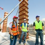 Students standing at construction site in hard hats and reflective vests.