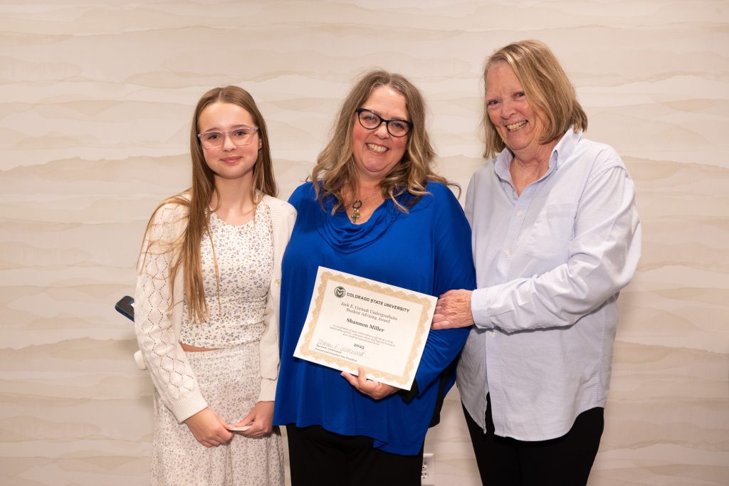 Shannon Miller holds award certificate with her mother and daughter on each side.