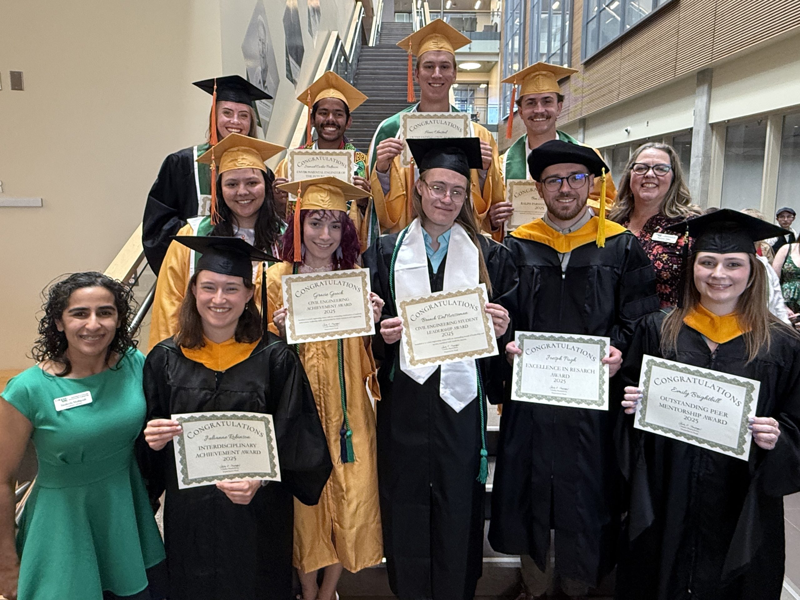 Group in graduation regalia pose with certificates.