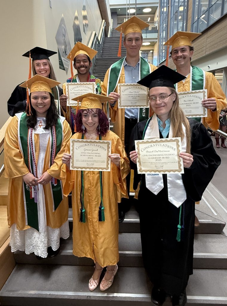 Students in graduation regalia stand holding certificates.