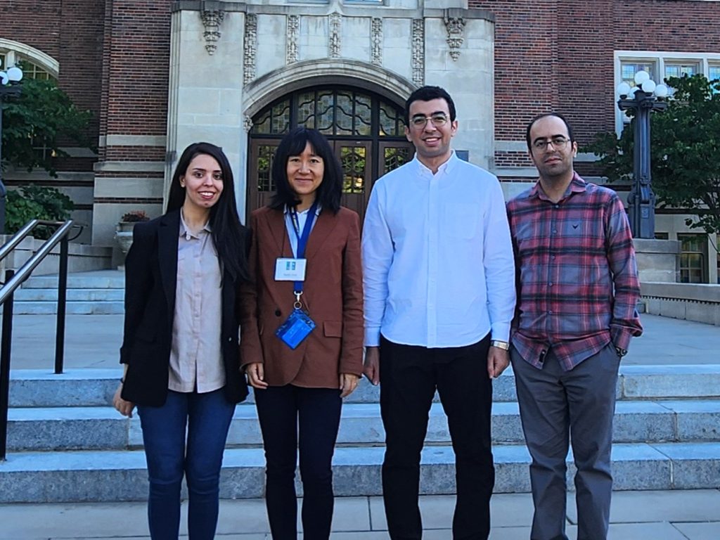Two women and two men stand outside in front of building on steps.