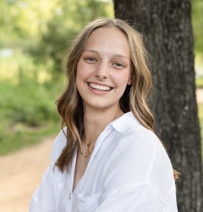 Woman in white shirt poses against tree.