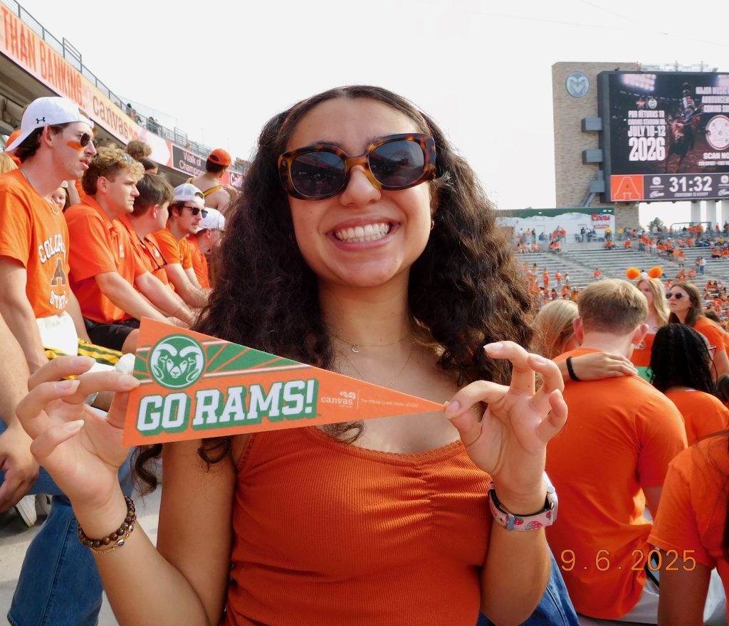 Woman in orange shirt and sunglasses holds pennant that reads "GO RAMS!".