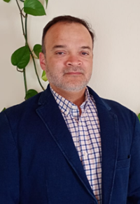 Man in suit stands for portrait in front of plant.