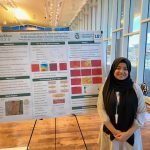 Woman in head covering stands at research poster.