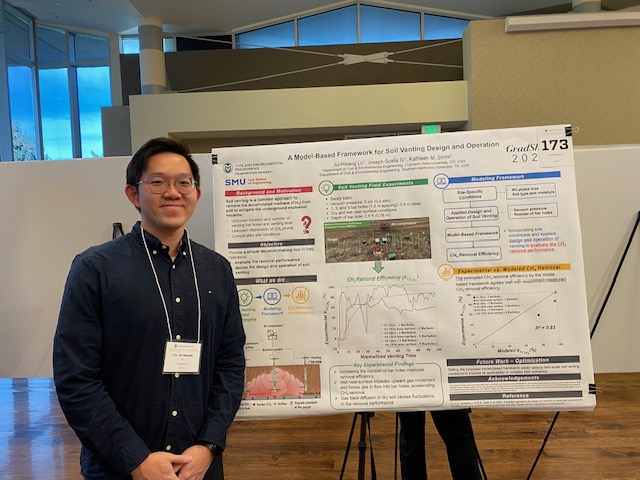 Man in blue shirt and lanyard stands by poster.