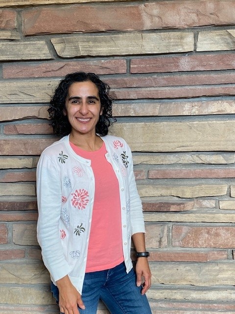 Woman in white cardigan leans against rock wall.