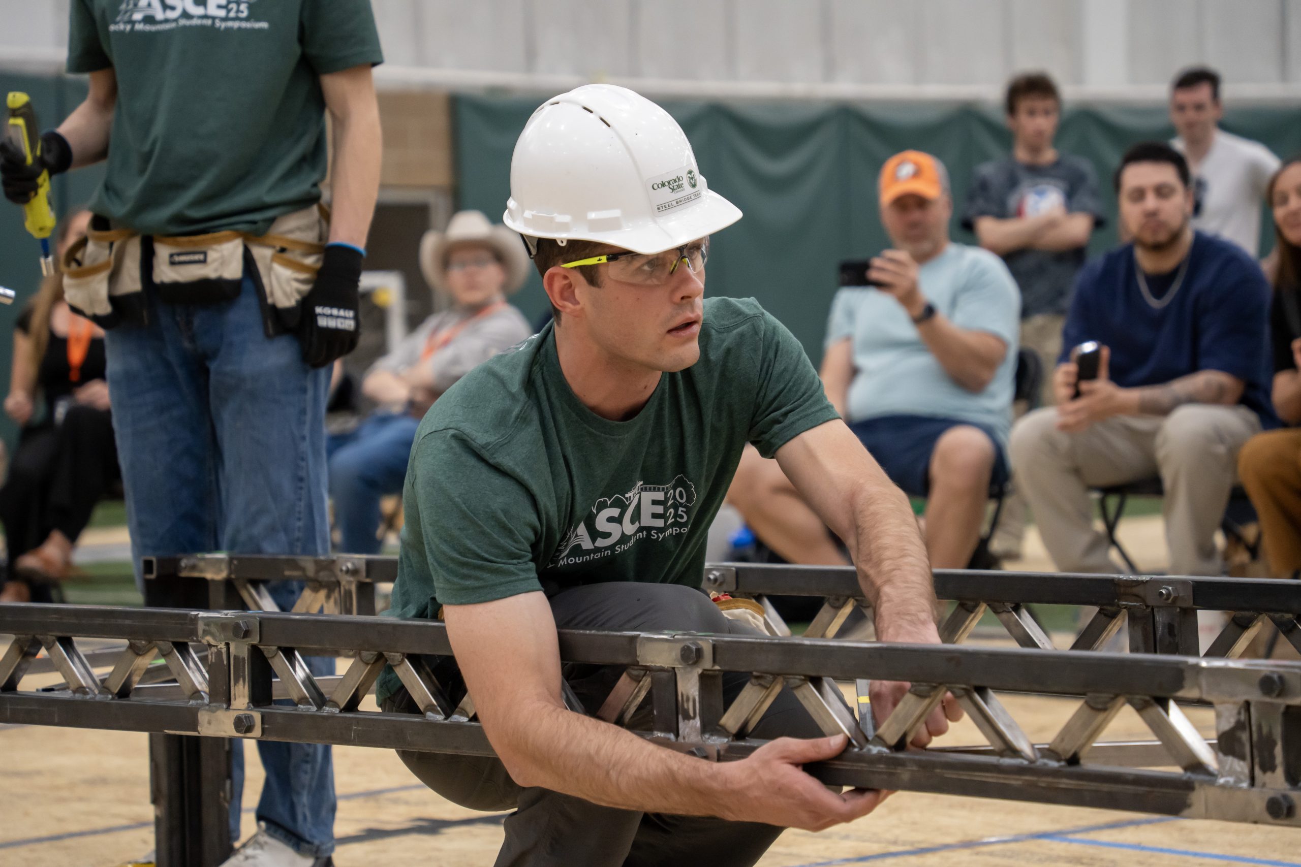 Man in white hard hat holds on to steel bridge.