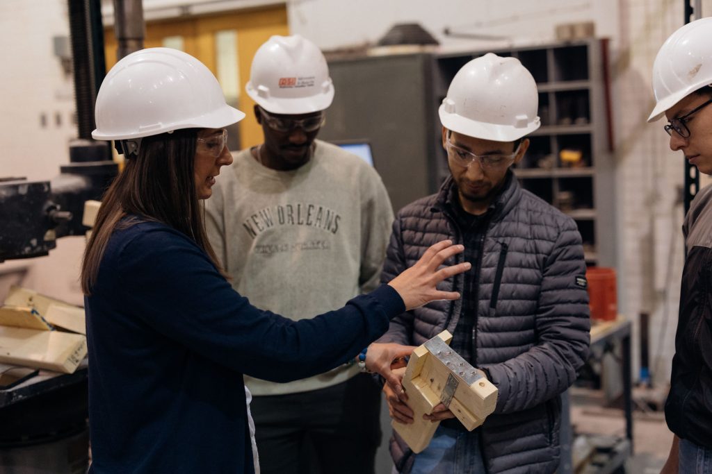 Woman in white hardhat speaks with students also wearing hardhats.