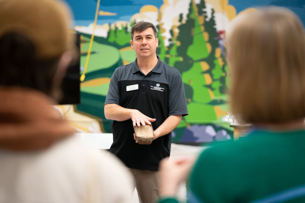 Man in black shirt with green mural background speaks to students.