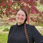 Woman in black stands in front of a tree with pink blooms.