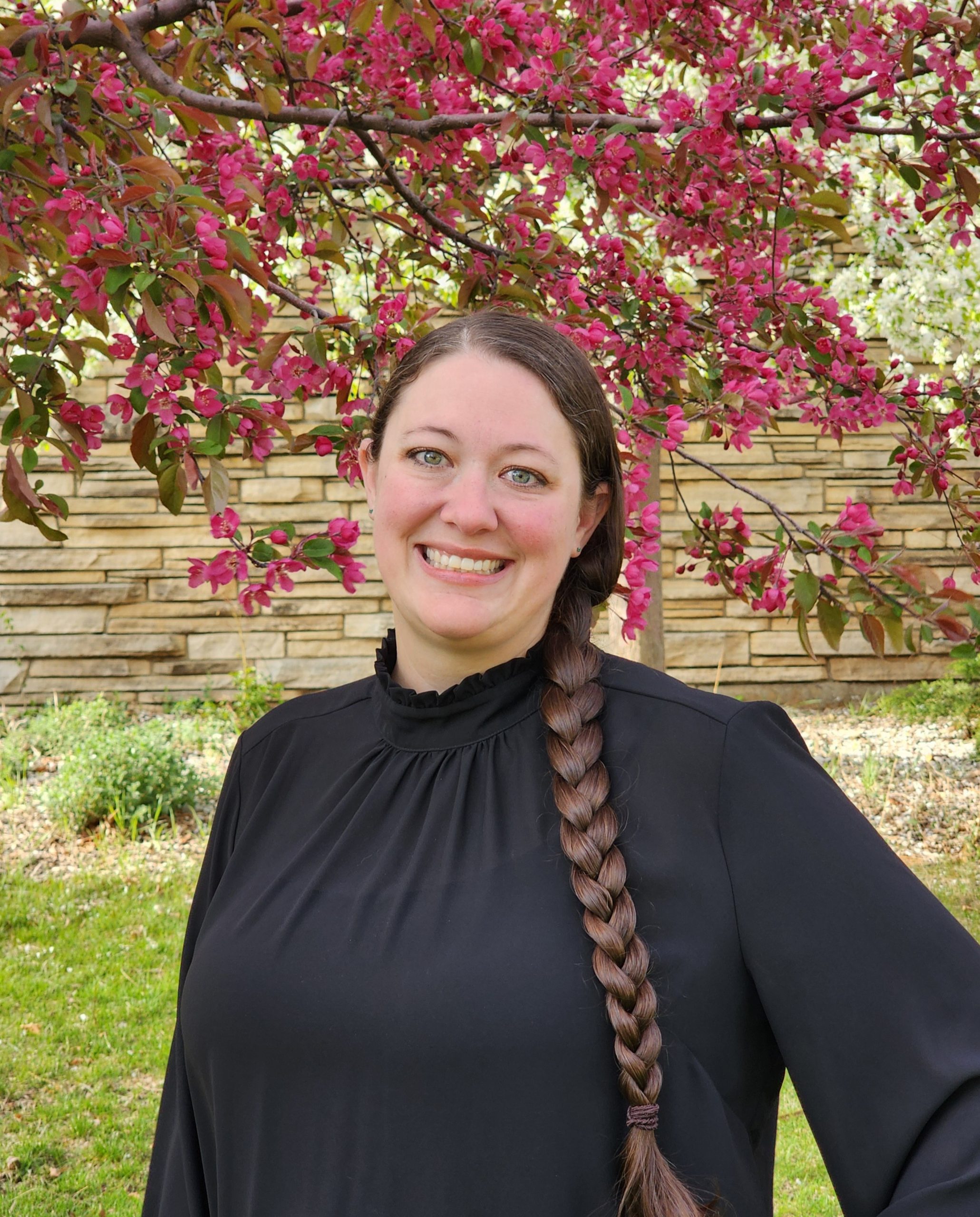 Woman in black stands in front of a tree with pink blooms.