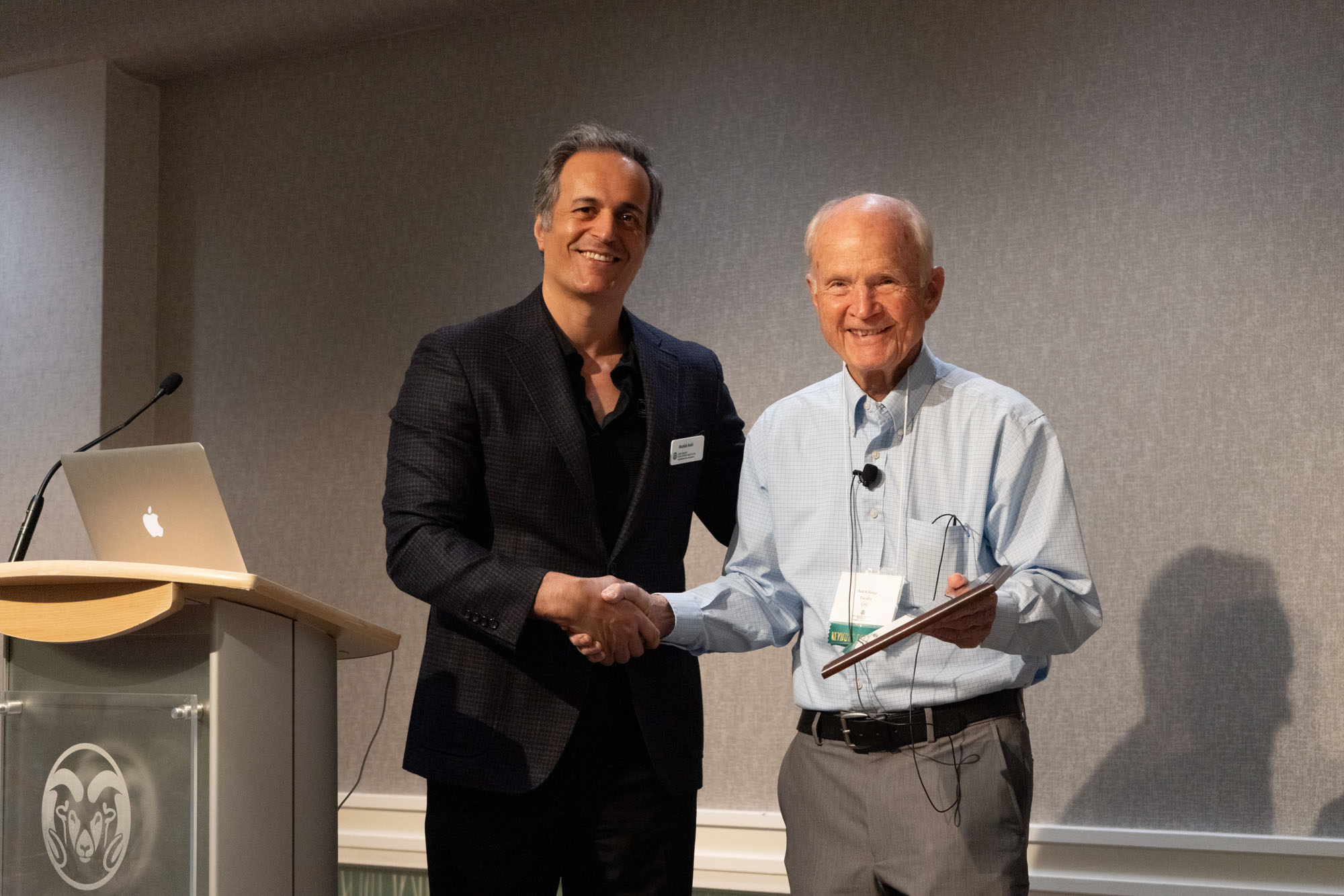 Two men shaking hands holding an award.