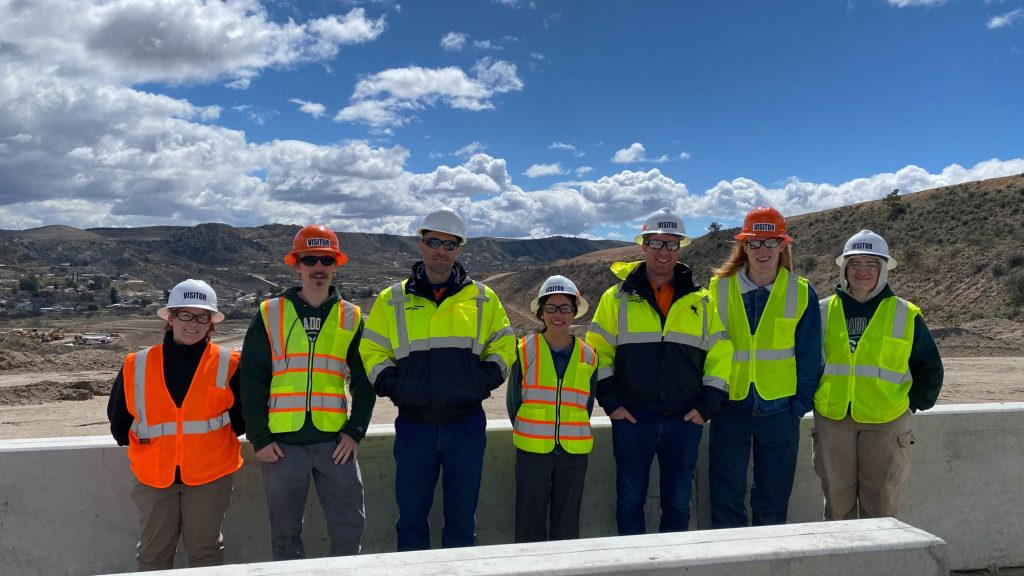 Students in safety vests and hard hats stand at mining site.