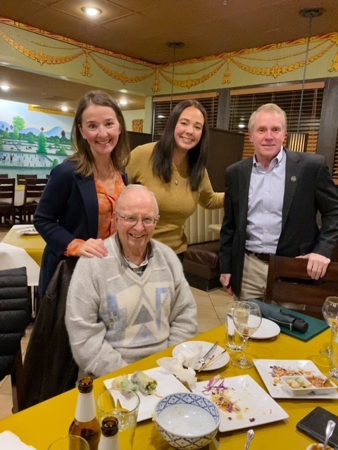 Three people behind man sitting at table at restaurant.