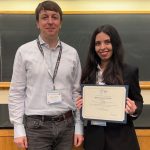 Man in white shirt stands with woman in blazer holding certificate.
