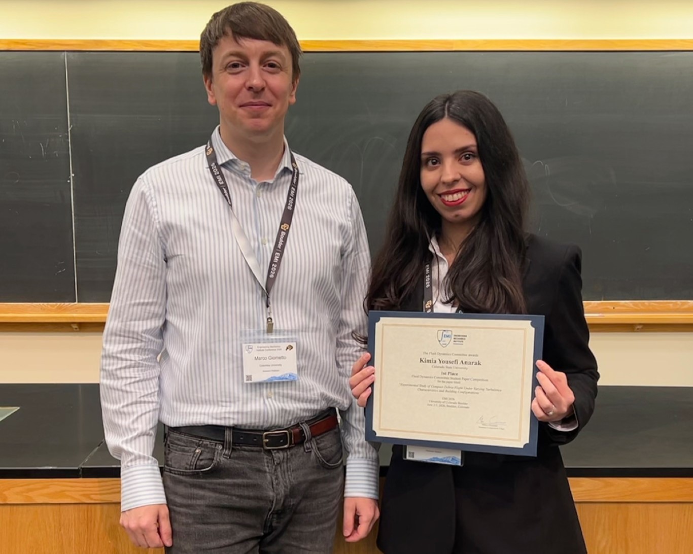 Man in white shirt stands with woman in blazer holding certificate.