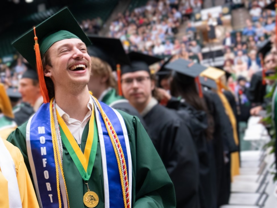 Student in green regalia smiles at camera.