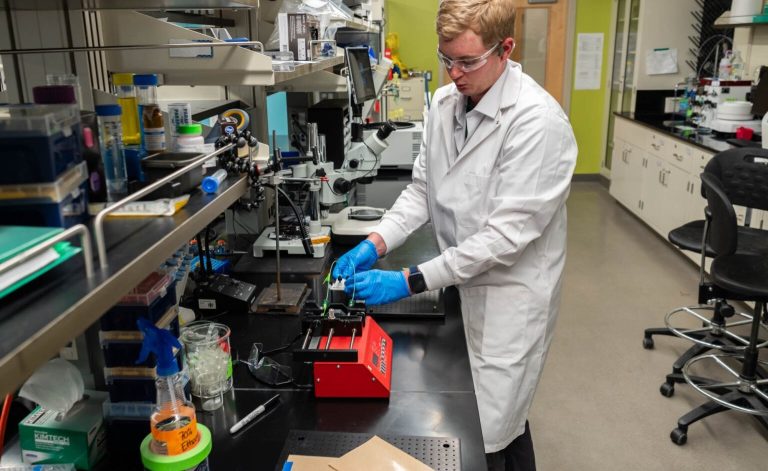 CSU environmental engineering student works in lab in white lab coat, googles, and safety glasses