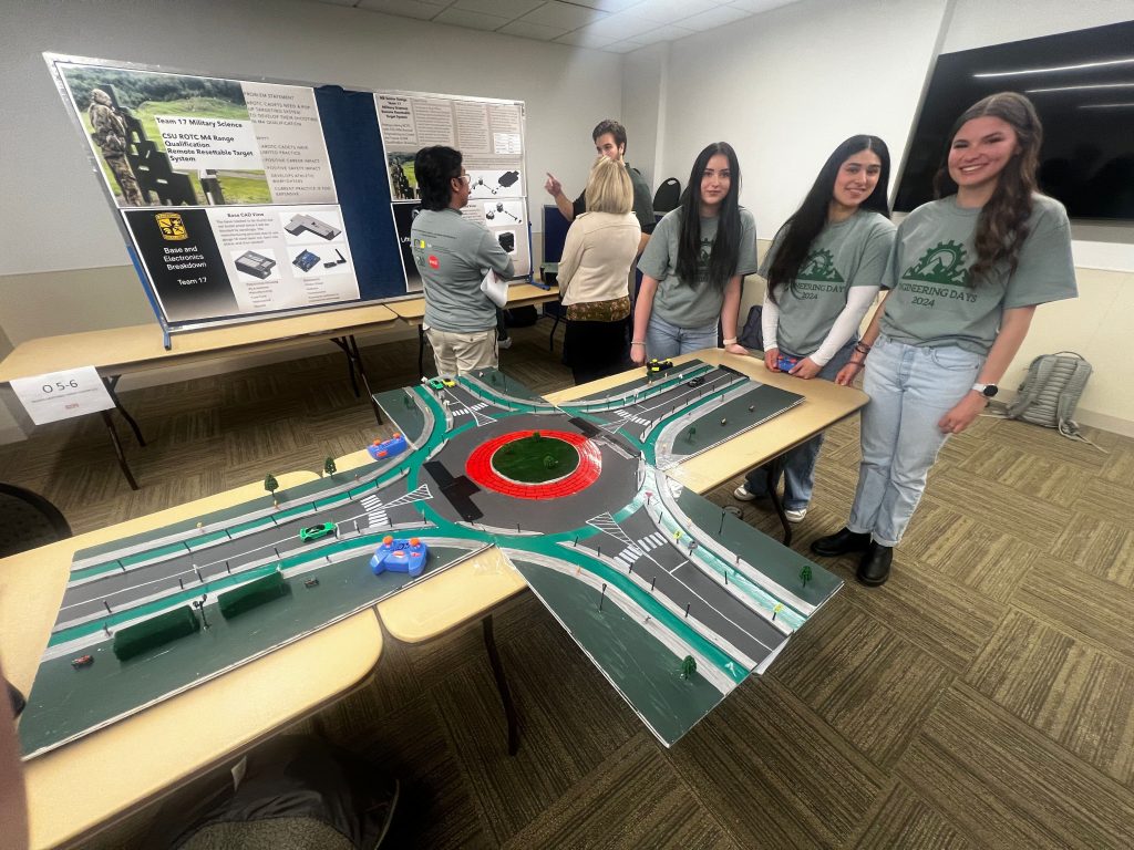 Three students showing a model roadway with roundabout using remote controlled cars.