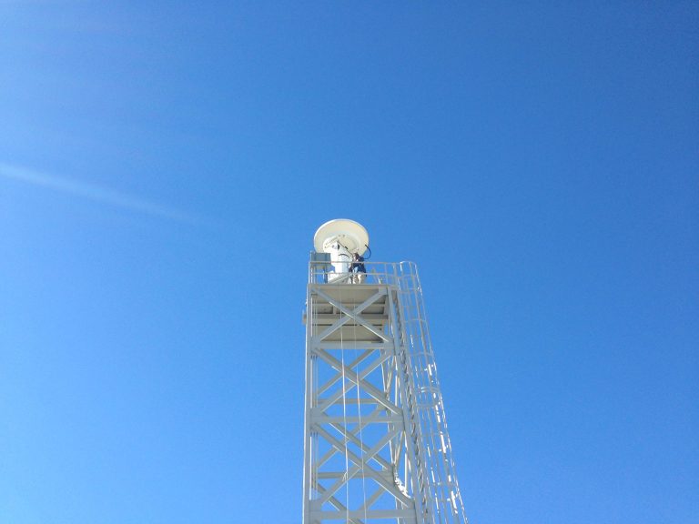 photo looking up at Dr. Chandrasekar and large radar on platform with blue sky in background