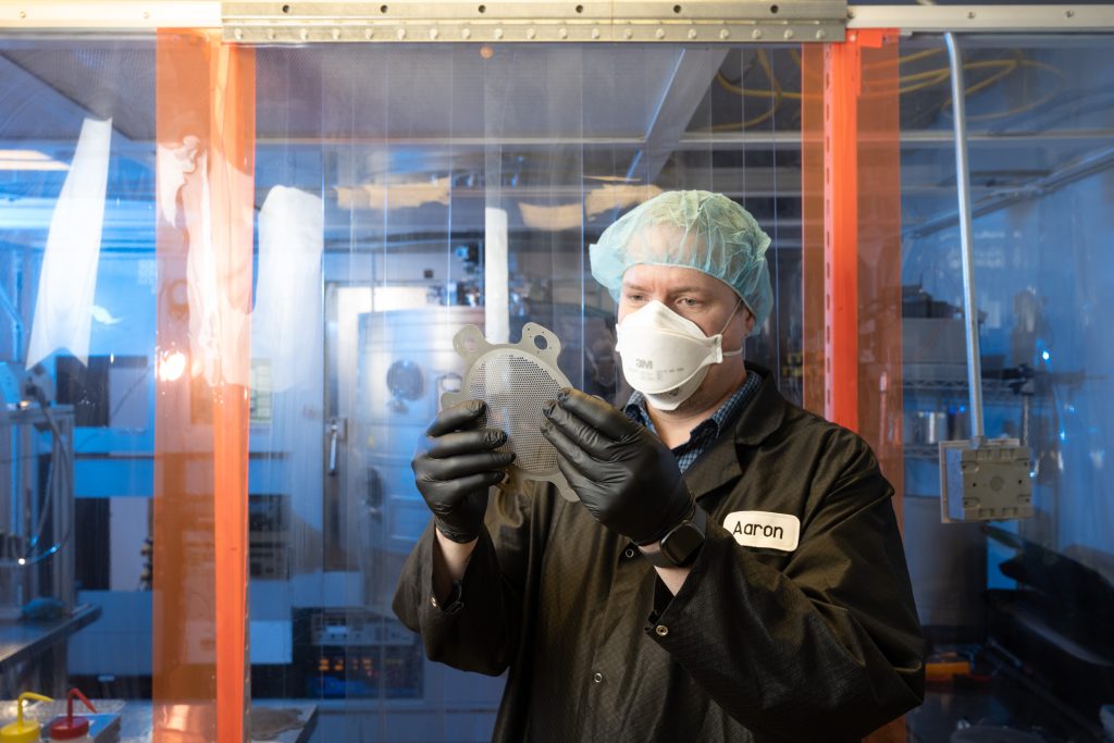 research student examining a part in the laser lab with equipment in background