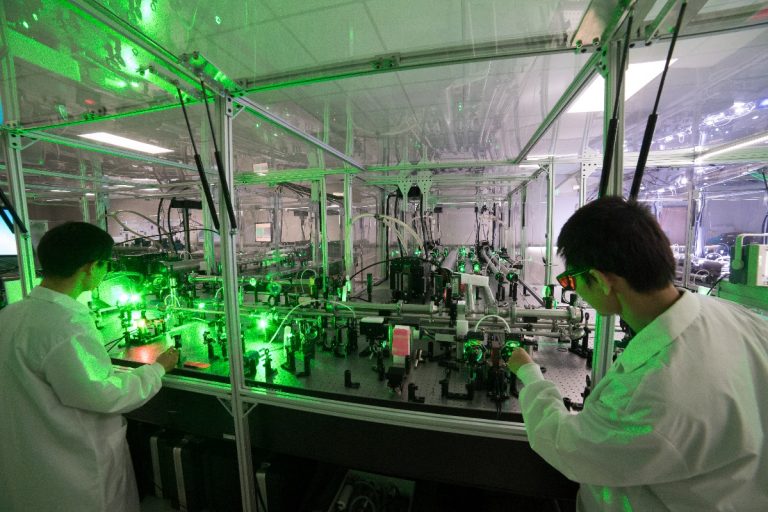 Two researchers working in laser lab with large display of equipment in background