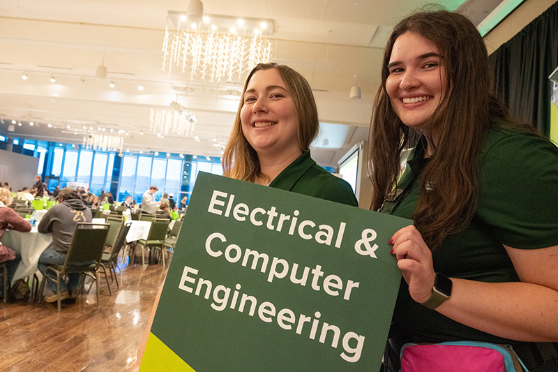 Two students ambassadors in CSU shirts holding Electrical & Computer Engineering sign with large group in background