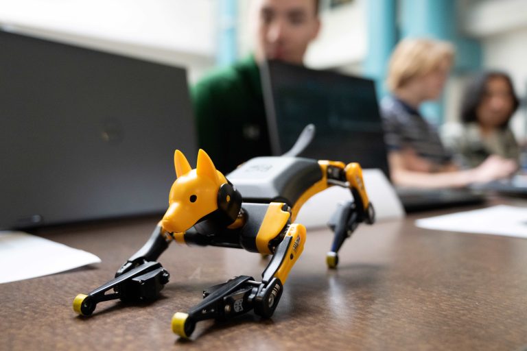 Close up of small dog robotic device, with students in background