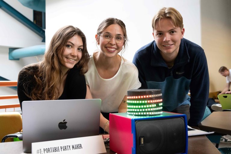 Three students smiling in front of bright engineering design project