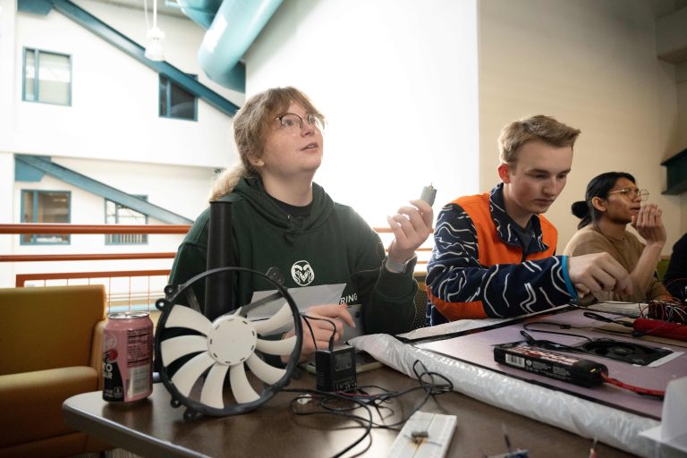 Woman sitting next to fan that's been converted into a design project, with two students working beside her