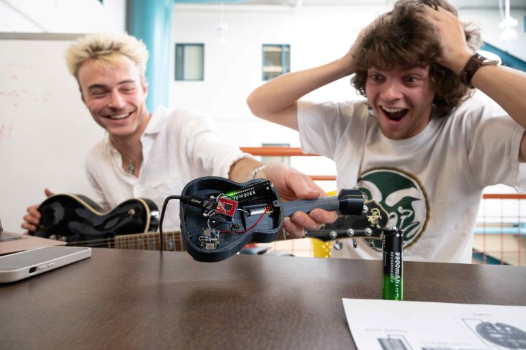 Close up of two students excitedly looking at project with guitar and electronics