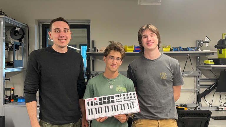 three males students, with one holding a synthesizer keyboard