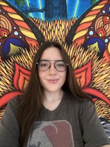 Lab member Isabella Gravante poses in front of a colorful tapestry with a fox design on it.