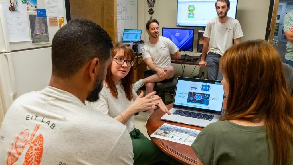 Dr. Jennifer Mulller explains the setup of an EIT system to Kim and Jay Norvell, using her laptop. Lab members Chris Rocheleau and Kyler Howard observe.
