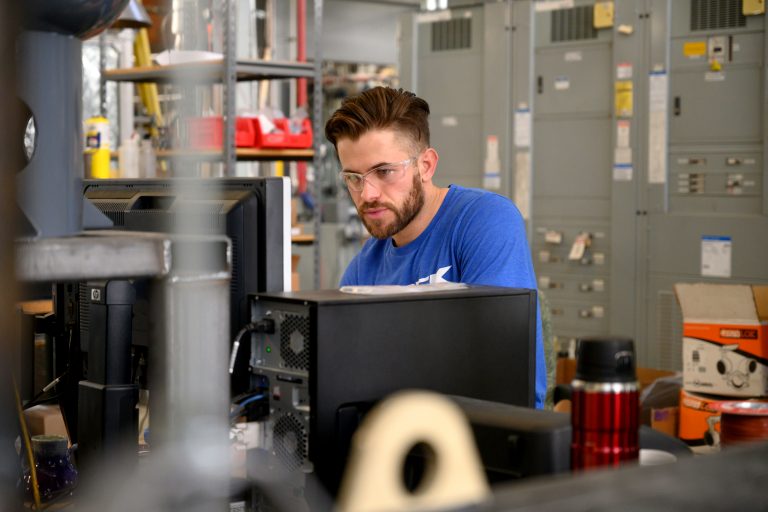 A male student sits behind a computer in a lab