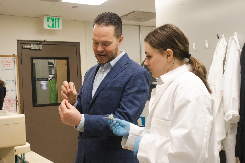 Faculty member talks with his hands to demonstrate concept to a female student in a lab coat.