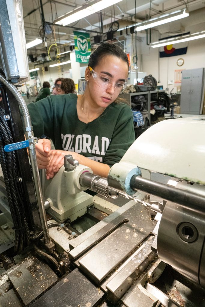 A female student works on a piece of engineering manufacturing equipment.