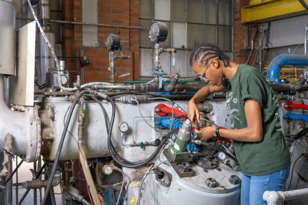 A female student works with tools on a large engine.