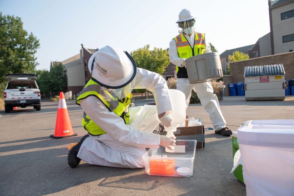 Two people in safety gear pouring liquid into beaker.