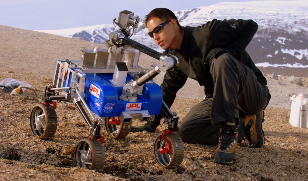 Paulo Younse kneeling in front of a JPL rover