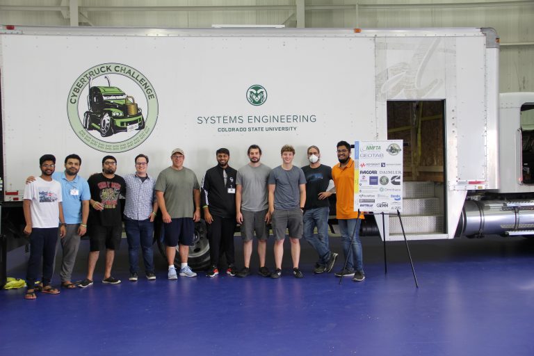 Group of students standing in front of a white truck with a green CSU Systems Engineering logo and CyberTruck challenge logo