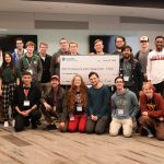 Students standing in a group and smiling with a large check in the middle addressed to the student winners of the challenge.