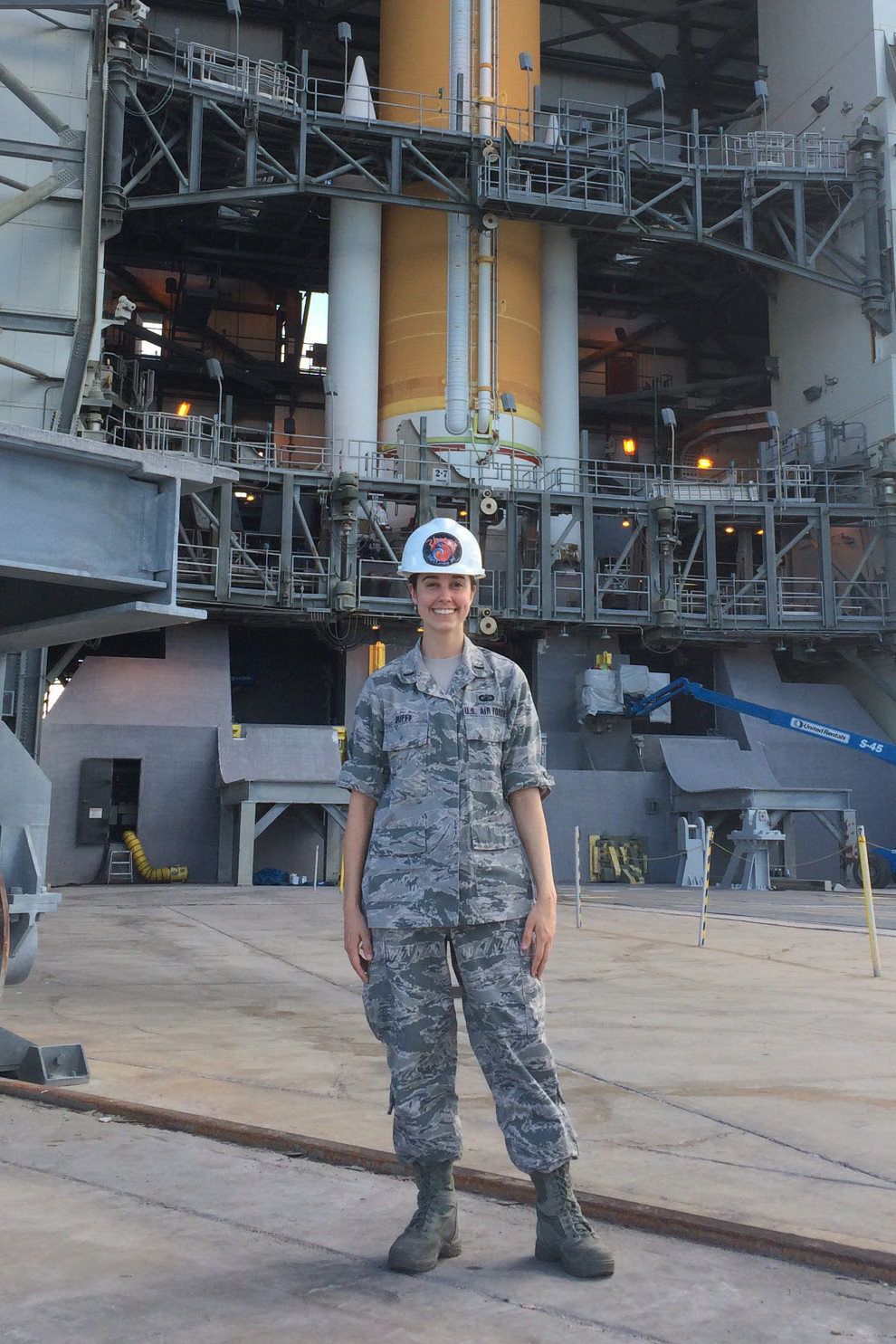 Laura Duffy in a hard hat and air force uniform standing in front of a rocket.