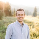 A young man stands outside in a summer landscape.