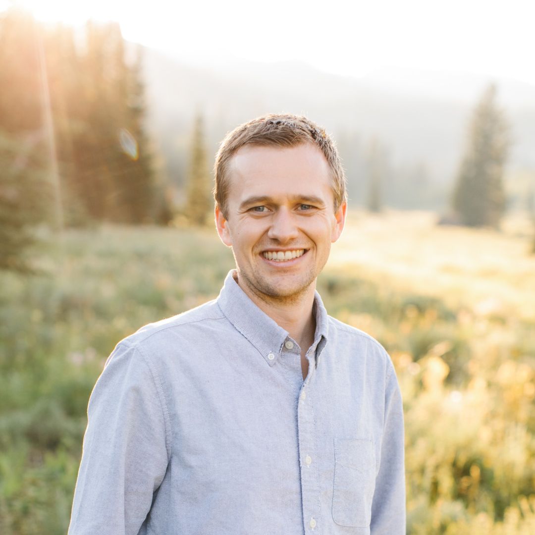 A young man stands outside in a summer landscape.